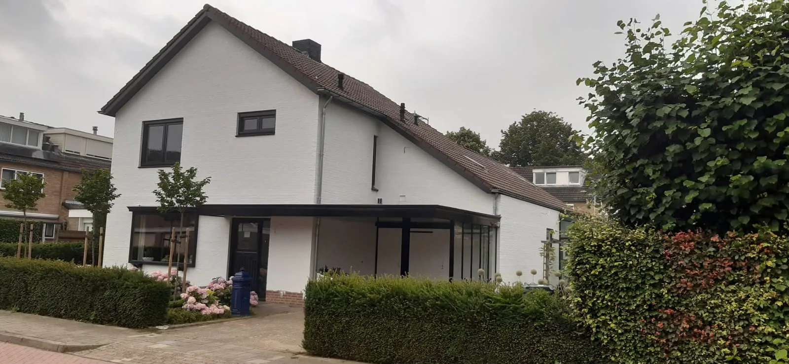 De woning na het schilderwerk: witte gevel, antracieten kozijnen en overkapping